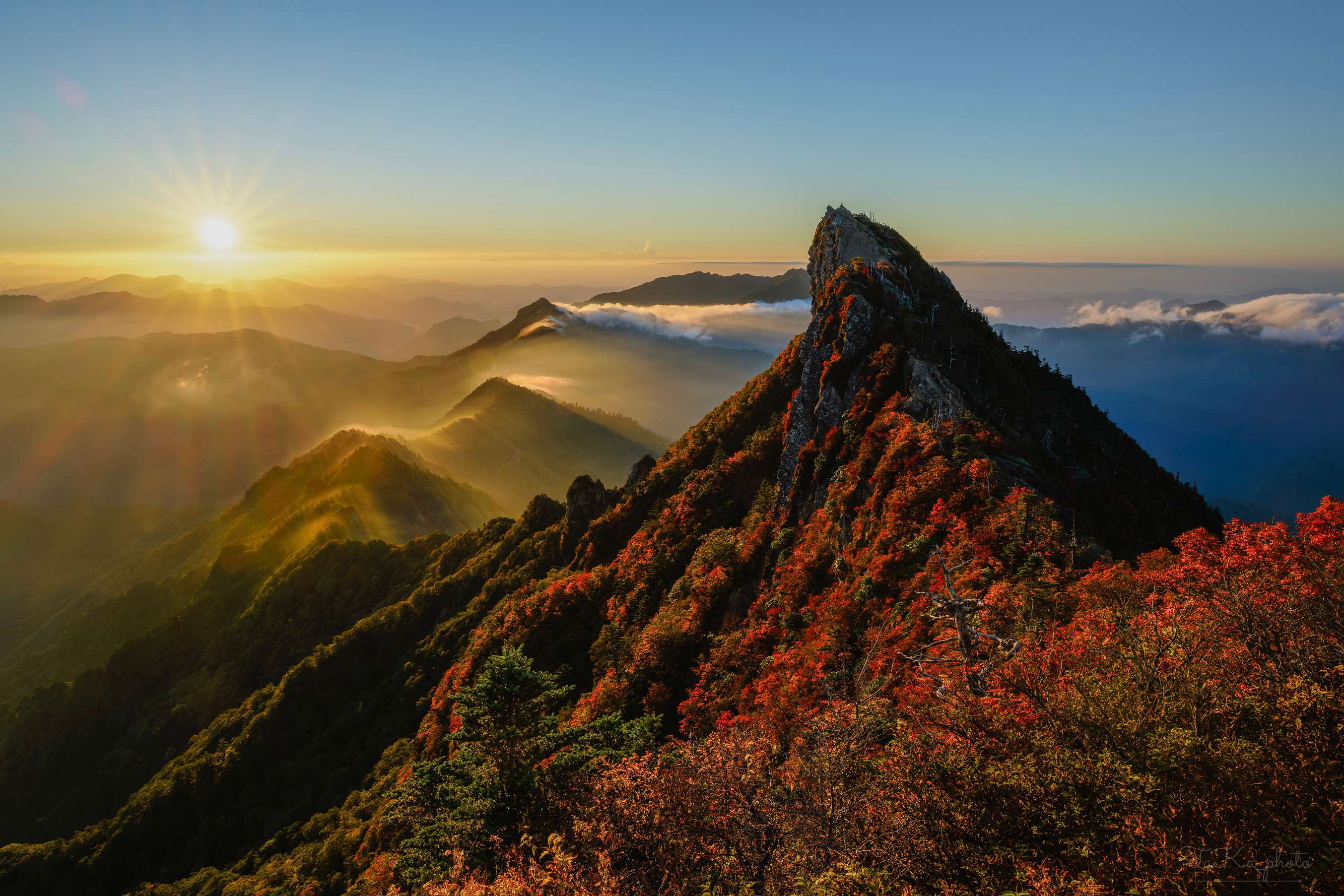 夜明けの光を受ける秋の石鎚山と紅葉